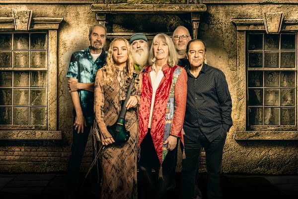 Six musicians, four men and the back and two women at the front, standing in front of a stately home.