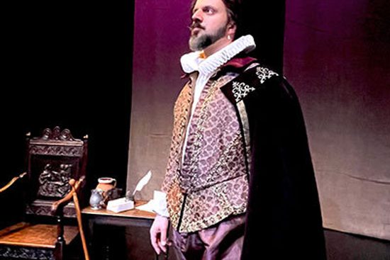 A man with brown hair and an earring wears purple elaborative Tudor style clothes and looks into the distance.