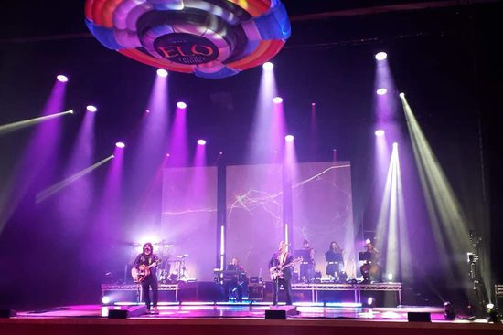 A band performing on stage with multiple purple spotlights on them.