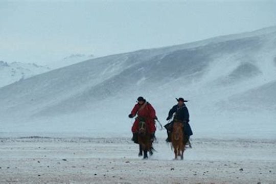 Two men on horses in a snowstorm.