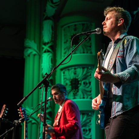 Two men singing and playing the guitar. The lights are green.