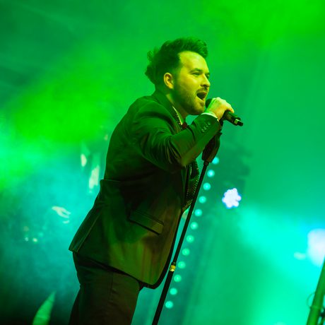 A man singing into a microphone on a stand. The lights around him and green.