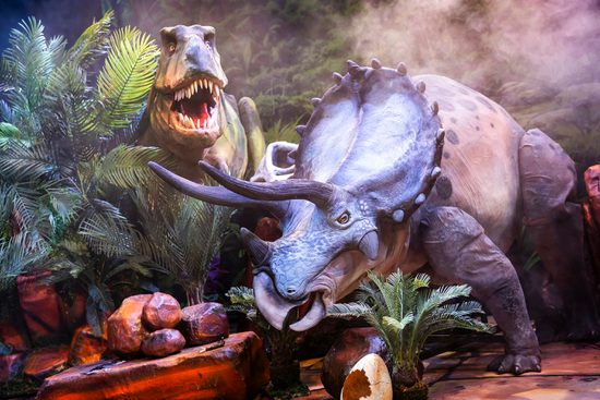 Two large dinosaur puppets standing in rocks and foliage.