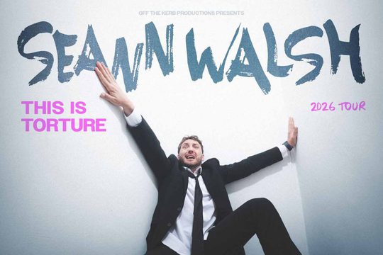 A man in a black suit looks as though he has fallen over against a grey background. He is holding onto the walls and looks scared. Text: Seann Walsh, This is Torture.