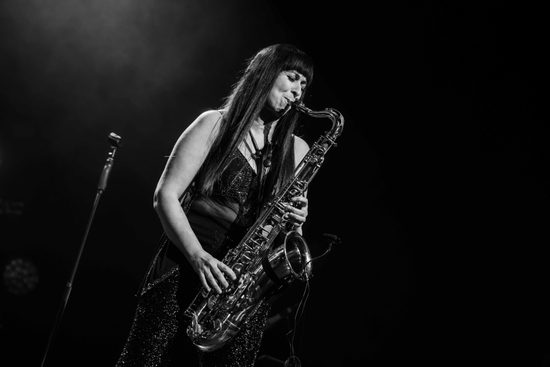 Black and white image of a woman with long straight hair playing the saxophone.