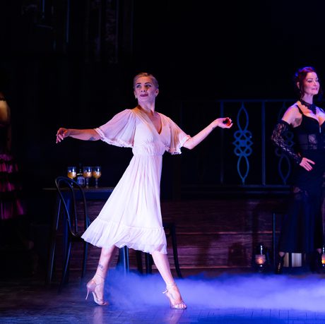 A woman in a light pink flowy dress dances on a stage.