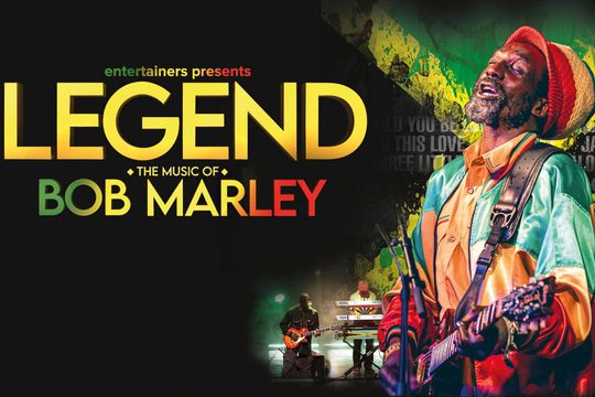 A black man in a hat and jacket that are red, yellow and green sings and plays guitar. Text: Legend: The Music of Bob Marley.