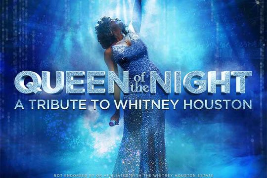 A woman in a silver dress with one arm in the air. She is lit by blue lighting.