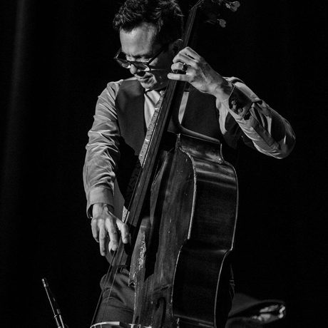 Black and white image of a man wearing glasses and a waistcoat playing the double bass.