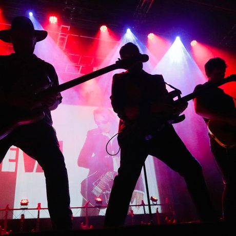 Silhouette of three men playing the guitar, a red light behind them.