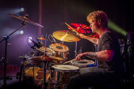 Blond man with tattoos plays the drums