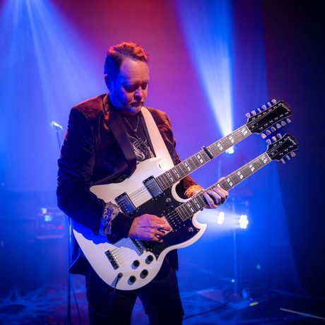 Man in a suit plays a double neck guitar.