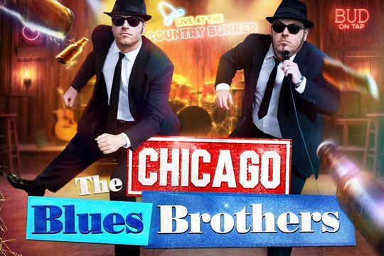 Two men in black suits, hats, and sunglasses dance in a country bar.