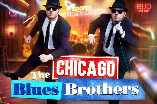 Two men in black suits, hats, and sunglasses dance in a country bar.