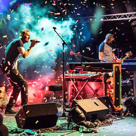 A singer and guitarist perform on a stage surrounded by colourful confetti.