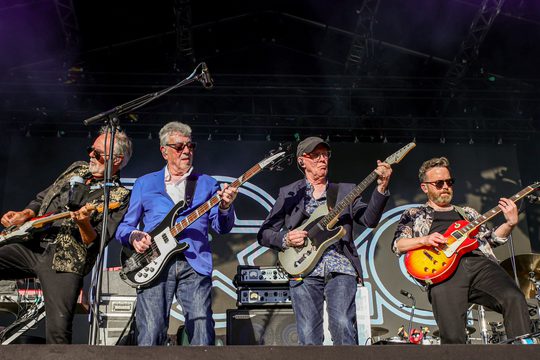 Four men play guitars at an out door festival.