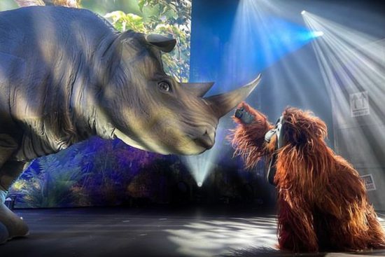 Realistic puppets of a rhino and an orangutan. The orangutan is reaching out to touch the horn of the rhino.