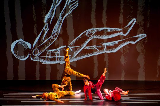 Four dancers, two in green and two in red, perform on a stage.