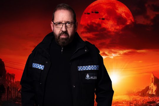A brunette man with a beard in a police uniform standing in front of a sunset with a red moon. There are three helicopters flying past.