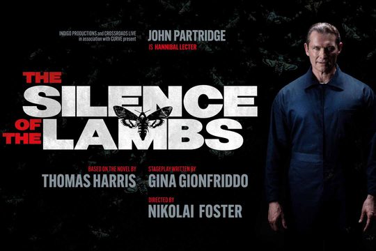 A white man in a dark blue jumpsuit stands and smiles menacingly. Text: The Silence of The Lambs. John Partridge is Hannibal Lecter.