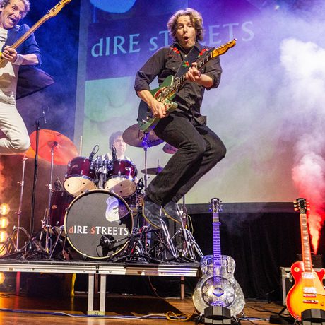 Two musicians play guitars and jump in the air.