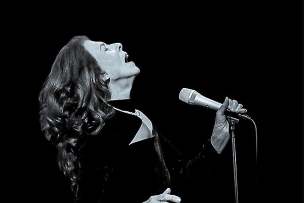 Black and white image of a woman with long hair singing into a microphone.