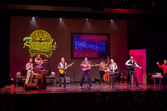 A group of 8 musicians play on a stage. They have various instruments including piano, guitar, drums, and double bass.