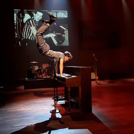 A man plays piano on stage and jumps so his feet are above his head.