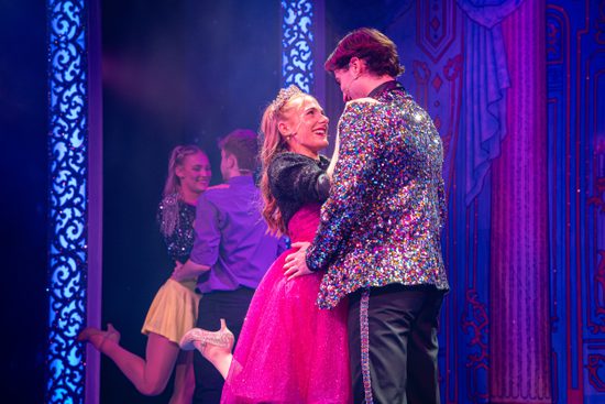 A girl in a pink dress and a man in a sparkly jacket embrace each other.