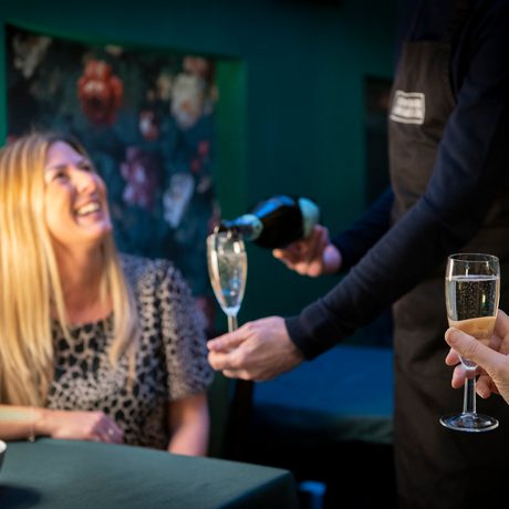 Woman looks up towards waiter and he serves her a glass of champagne