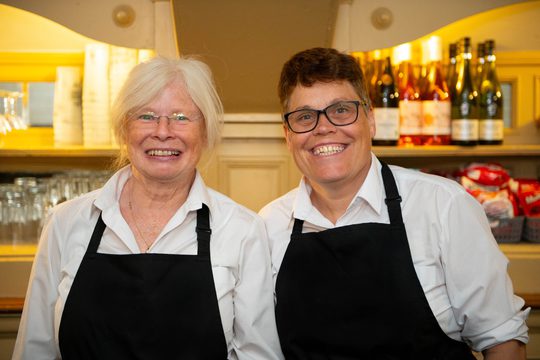 Two volunteers smiling at the camera in white shirts and black aprons
