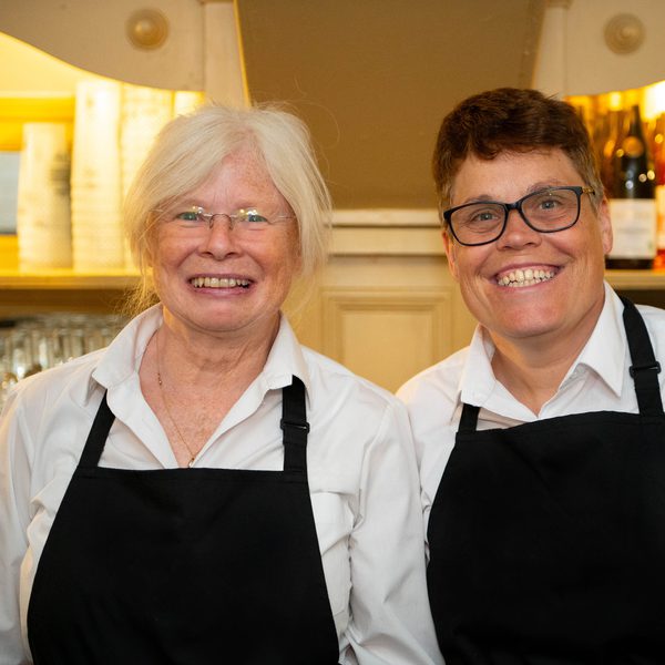 Two volunteers smiling at the camera in white shirts and black aprons