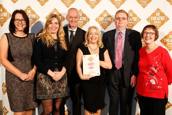 Six members of staff pose with a plaque