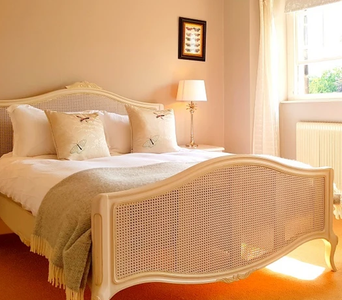 Double bed with delicate headboard on wooden floors, with window to the right letting in bright sunlight